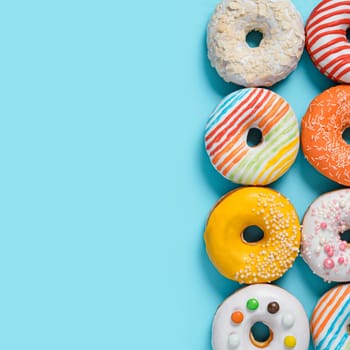 Delicious glazed donuts on blue background. Square flat lay - set of different colorful donuts or doughnuts on blue with copy space for text or design. Bright sun light with hard shadows.