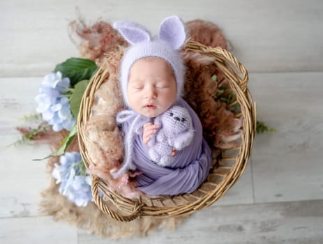 Newborn Girl In Pink Suit With Toy Cat Sleeps In Wooden Heart-Shaped Bowl During Professional Newborn Photoshoot