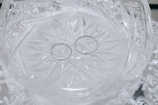 There are two white gold rings in a crystal plate. The concept of a wedding and a holiday.
