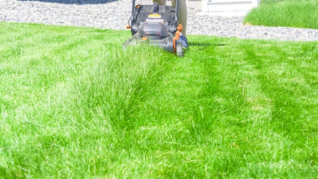 Castle Rock, Colorado, USA-June 25, 2023- At a residential suburban house, a lush green lawn is meticulously mowed using an electric lawn mower, creating a well-manicured and inviting outdoor space.