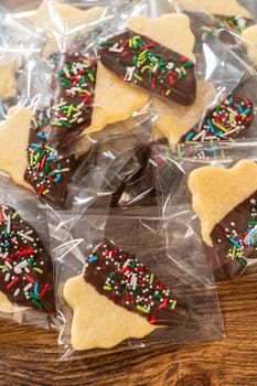 Carefully packaging Christmas cutout cookies, half-dipped in chocolate and presented in clear cellophane wrapping, perfect for festive gifting.