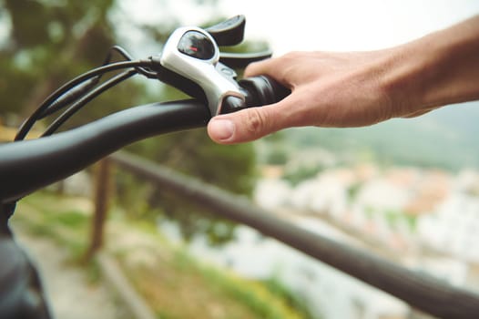 Close-up man cyclist puts hands on brakes, squeezing then while descending during his trip on electric bike in the mountains. People. Active healthy lifestyle. Ecologically friendly mode of transport