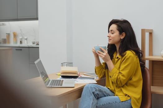 Thoughtful young woman in eyewear using computer while sitting on the sofa at home. High quality photo