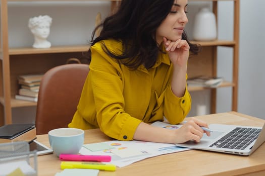 Thoughtful young woman in eyewear using computer while sitting on the sofa at home. High quality photo