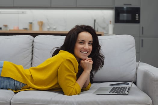 Thoughtful young woman in eyewear using computer while sitting on the sofa at home. High quality photo