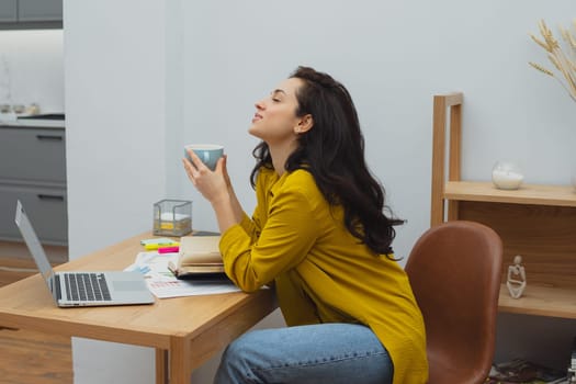 Thoughtful young woman in eyewear using computer while sitting on the sofa at home. High quality photo