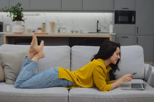 Thoughtful young woman in eyewear using computer while sitting on the sofa at home. High quality photo