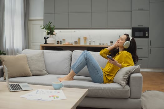 Thoughtful young woman in eyewear using computer while sitting on the sofa at home. High quality photo