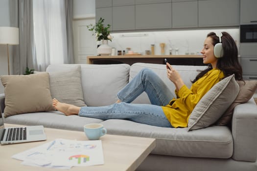 Thoughtful young woman in eyewear using computer while sitting on the sofa at home. High quality photo