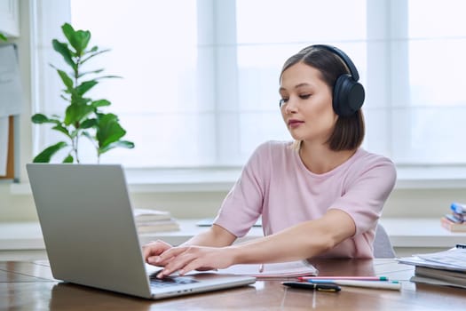 Young female in headphones using computer laptop for studying, university college student studying at home, writing typing. Technology, education, training, youth concept