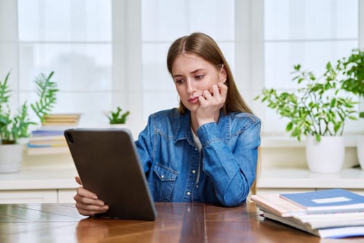 Young teenage female student sitting at home looking talking in web camera of digital tablet. Girl teenager 16,17,18 years old studying remotely, video conference call, e-learning technology education