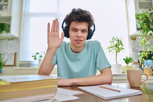 Webcam view of college student guy wearing headphones, talking looking at camera, sitting at desk in home. Young male studying online, video chat call conference, e-learning technology education