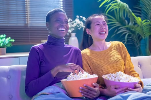 Two girl friends sitting on the couch watch a movie and eat popcorn. Funny friends relaxing together. High quality photo