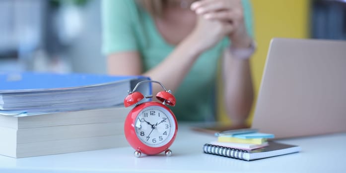 Woman sits at workplace next to alarm clock at ten in morning. Start of the working day concept