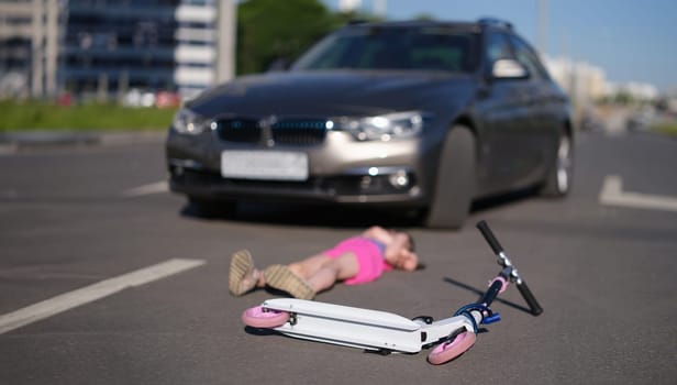 little girl lies on asphalt with scooter after collision with car. Hitting child on the road concept