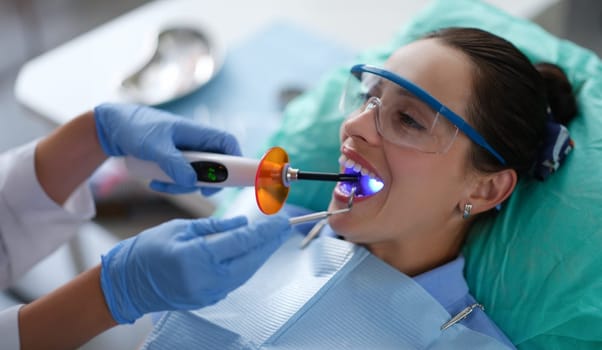 Dentist holds LED dental lamp and instrument in patient mouth. Dental services concept