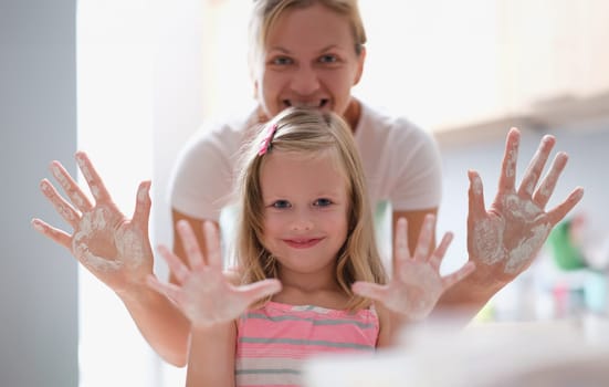 Mom and little girl showing palms of hands in flour. Teaching children to cook food concept