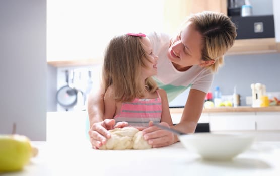 Little girl and mom making dough pie at home. Child care concept