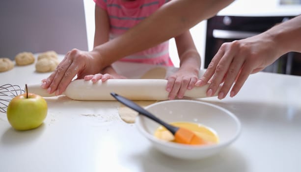 Mother and daughter rolling out flour dough at table closeup. Joint leisure with children concept