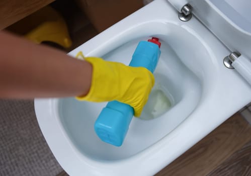 Woman hand pours cleaning agent into toilet bowl. Household chemicals for cleaning toilets concept