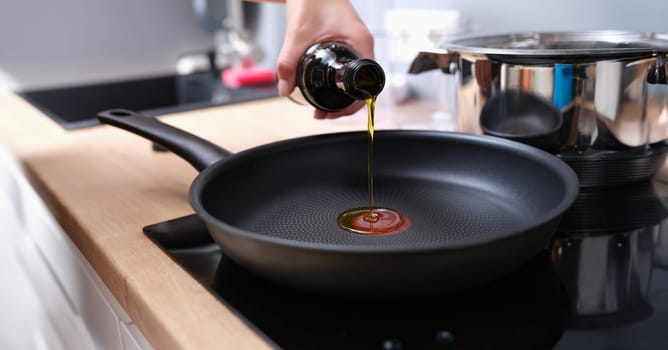 Chef pouring olive oil into frying pan in kitchen closeup. Healthy eating concept