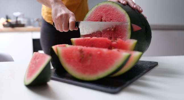 Woman cutting watermelon with kitchen knife at home closeup. Vegetarian food concept