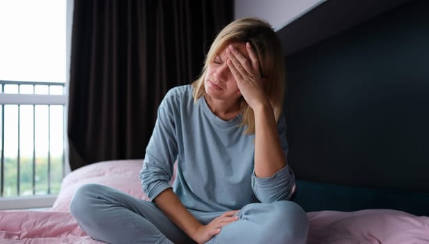 Young sick woman in pajamas sitting in bed and holding her head. How to deal with insomnia concept