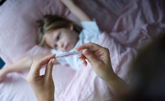 Woman hand holding mercury thermometer with high temperature against background of sick girl closeup. Seasonal colds in children concept