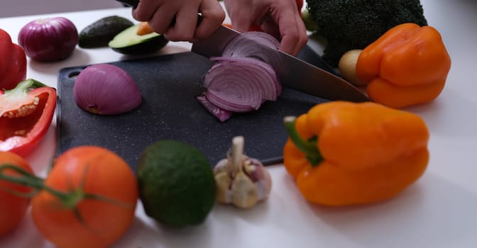 Chef cutting red onion on board among vegetables closeup. Recipes for cooking dishes from farm products concept