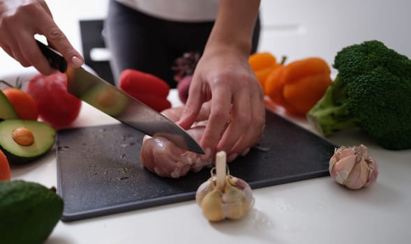 Chef cutting meat on board near vegetables closeup. Healthy nutritious food concept