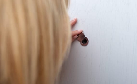Woman opens and looks through peephole. Peephole in steel entrance door concept