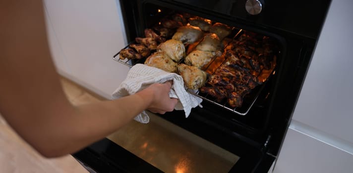Woman taking out grill of baked chicken from oven closeup. Recipes for cooking in oven concept