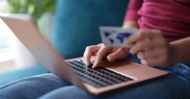 Woman typing on laptop keyboard and holding credit bank card in her hands closeup. Online payments concept