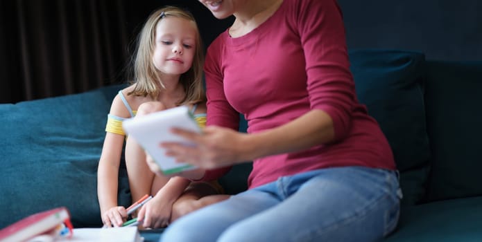 Little girl and woman sitting on couch with textbooks. Home education concept