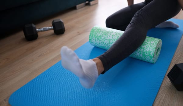 Woman sitting on rubber mat and training with roller closeup. Muscle stretching concept