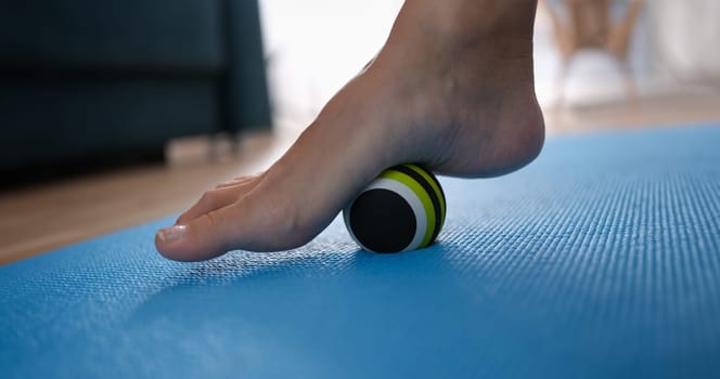 Woman leg rolling ball on foot at home closeup. Prevention and treatment of flat feet concept