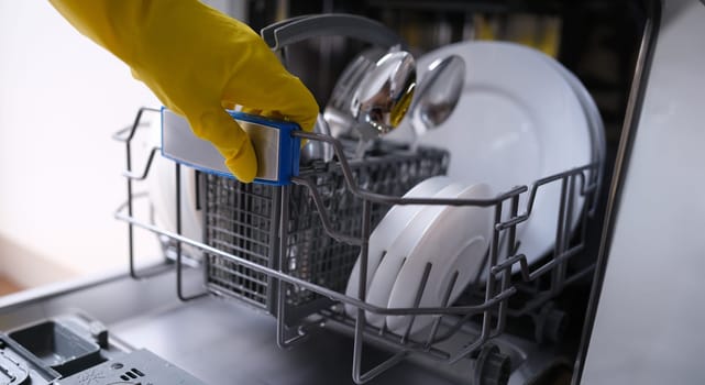Housewife in rubber gloves getting clean dishes out of dishwasher closeup. Sale and service of household appliances concept