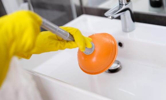 Plumber with rubber gloves cleaning sink with plunger in bathroom closeup. Husband for hour concept
