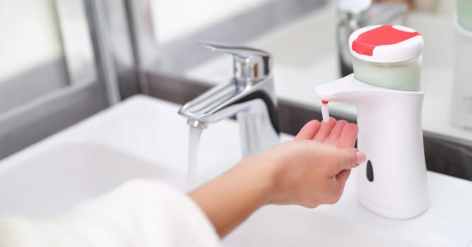 Woman picking up liquid soap from hand dispenser in bathroom closeup. Modern hygiene technologies concept