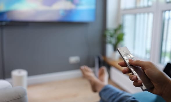 Woman is sitting on sofa and holding TV remote control in her hands closeup. Home leisure and entertainment concept