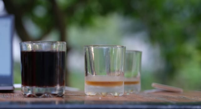 Two transparent glass glasses full of dark liquid and empty stand on table. Drinking drinks in summer cafes concept