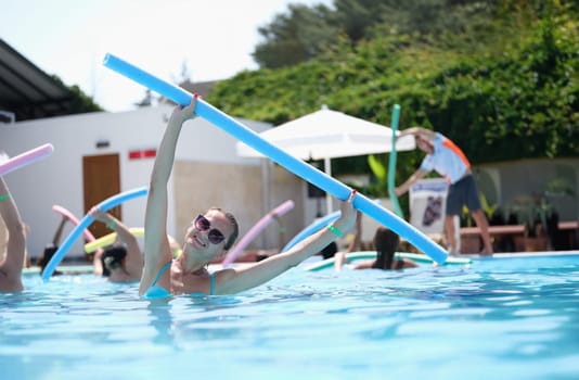 Attractive woman doing exercises with noodles is engaged in aqua aerobics. Benefits of sports exercise in water concept