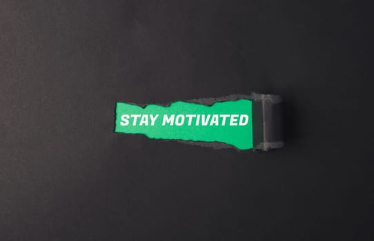 A green sign that says Stay Motivated. It is torn in half. The sign is on a black background