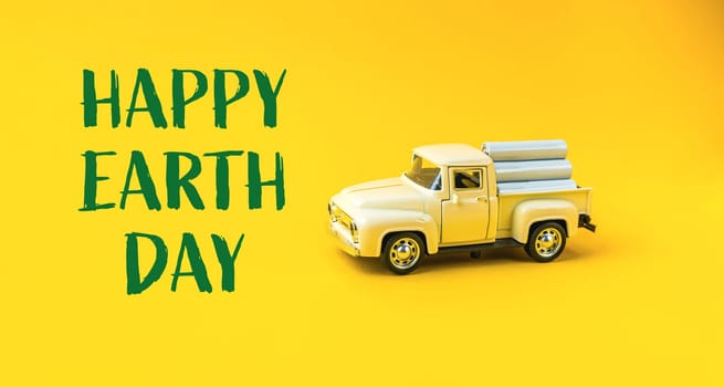 A toy truck is on a yellow background with the words Happy Earth Day written below it. The truck is surrounded by a pile of wood, which could symbolize the importance of preserving natural resources