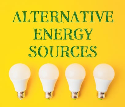 A yellow background with four white light bulbs on it. The words alternative energy sources are written in green