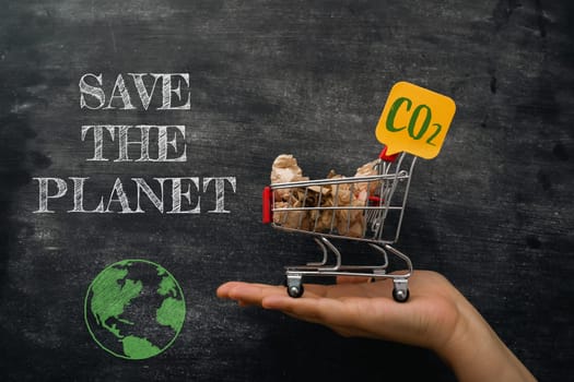 A hand holding a shopping cart with a sign that says Save the Planet. The cart is filled with items that are labeled with CO2