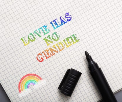 A rainbow is on a piece of paper with the words love has no gender written underneath it. A black marker is next to the rainbow