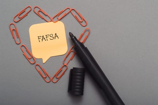 A pen with a piece of paper with the word FAFSA written on it. The pen is surrounded by paper clips, creating a heart shape