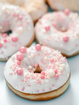 Delicious tender donuts glazed white glaze and sprinkled with pink pearl dressing. Idea decorating donuts for wedding, romantic event, celebration. Selective focus with copy space. Vertical