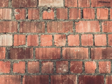 A brick wall with a rough texture and a faded red color. The wall is made of bricks and has a worn appearance